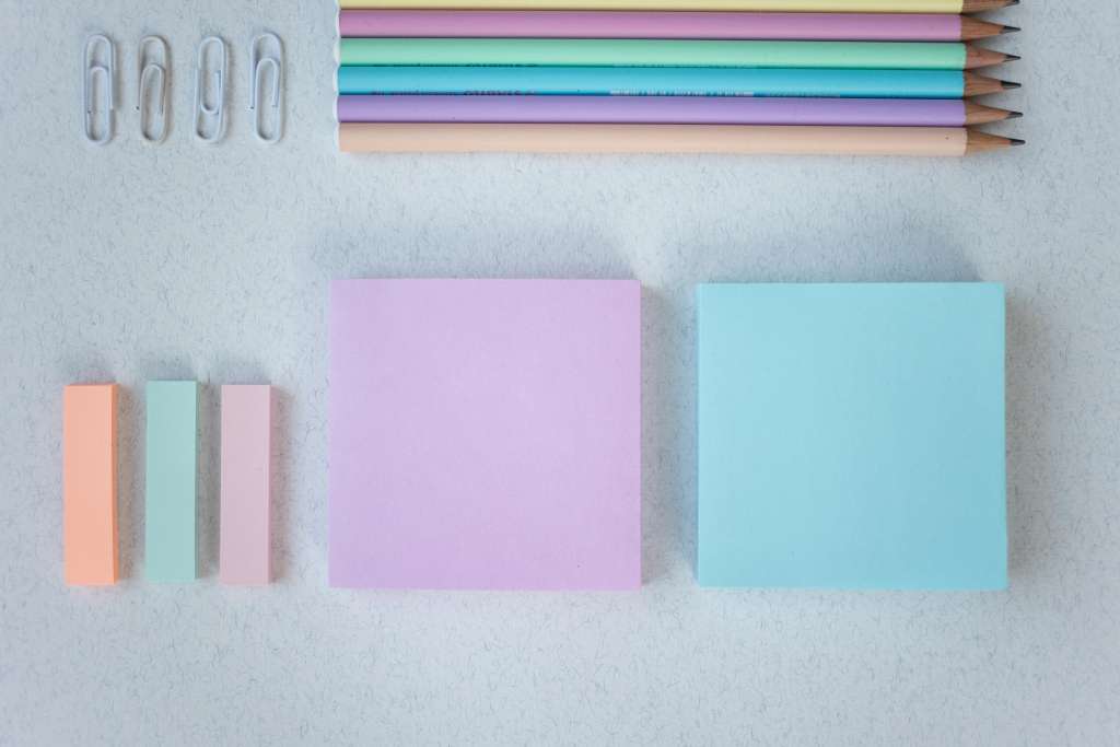 Büroklammern, Stifte, Post-Its in klein und in quadratisch, alles in Pastellfarben auf weißem Hintergrund.