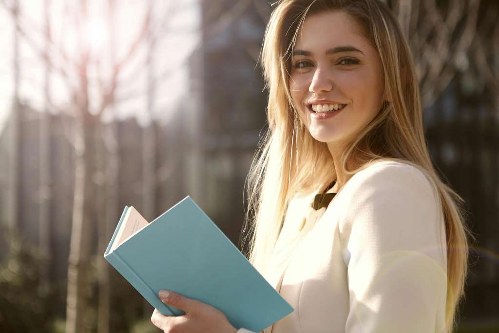 Lächelnde Frau mit aufgeschlagenem, türkisfarbenem Buch in der Hand