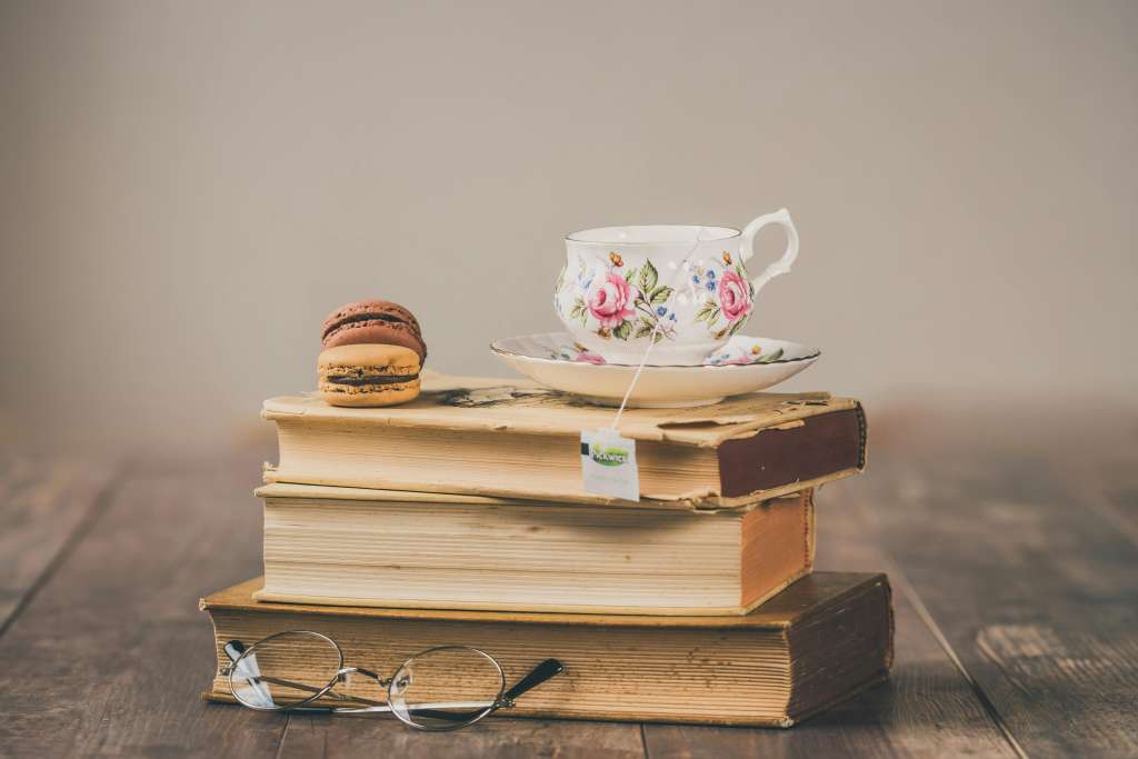 Gestapelte alte Bücher mit einer Vintage-Tasse und Macarons – ein gemütliches Setting, das an das Lese- und Schreiberlebnis von Selfpublisher-Autorinnen erinnert.